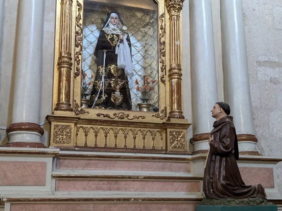 Staty av en böneman på hans knän framför statyn av nunnan i en katolsk kyrka i Peru