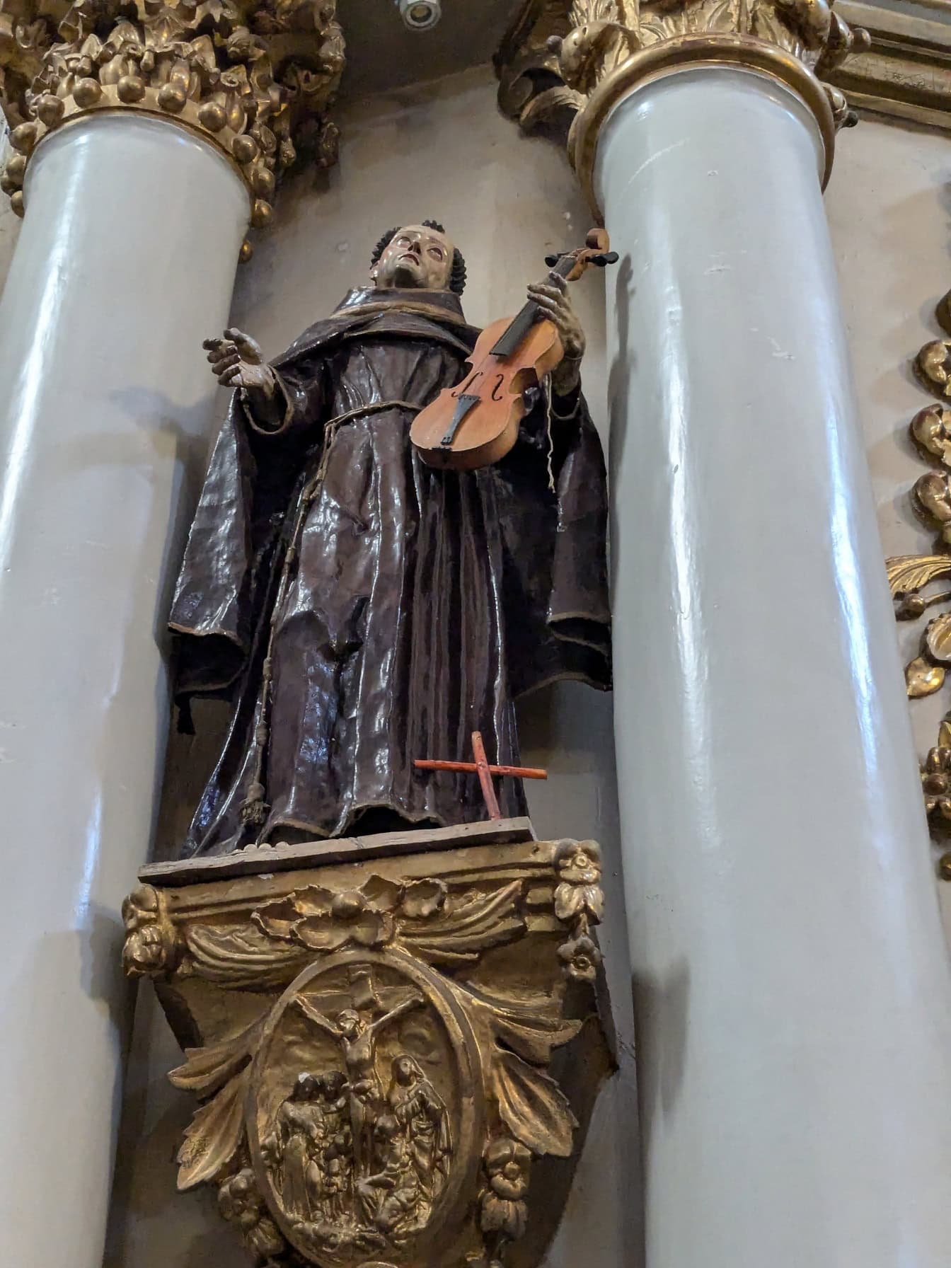 Staty av ett helgon som håller en fiol mellan kolonner i kyrkan