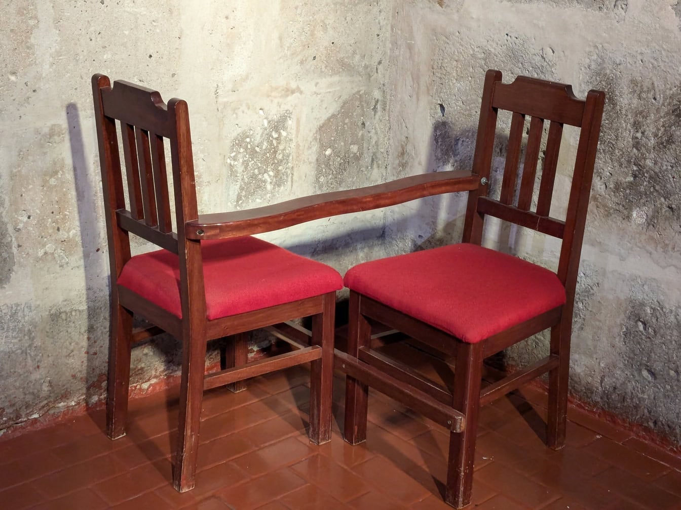 Dwa połączone ze sobą drewniane krzesła z czerwonymi poduszkami, które służą do celów religijnych w rogu kościoła katolickiego