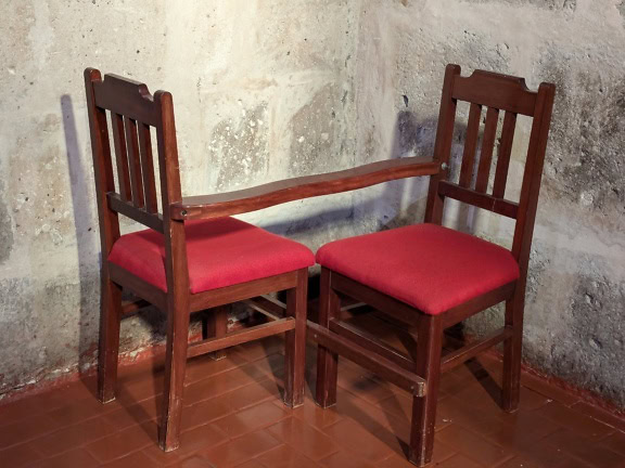 Dve spojené drevené stoličky s červenými vankúšmi, ktoré sa používajú na náboženské účely v rohu katolíckeho kostola
