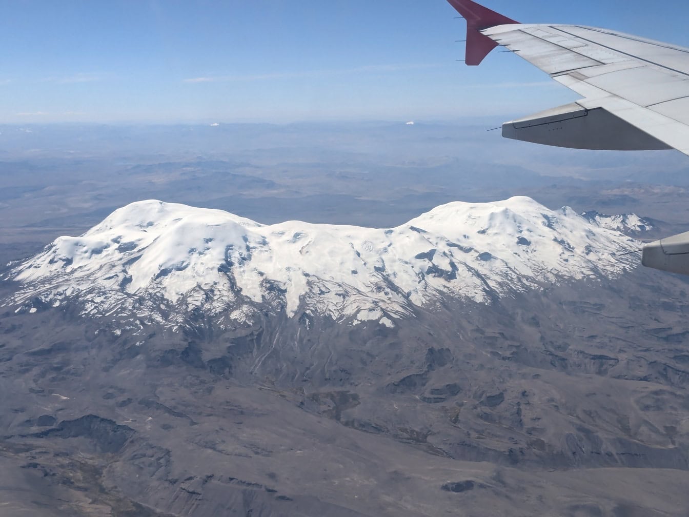 从飞机上拍摄的照片，前景是飞机机翼，背景是位于秘鲁中东南部安第斯山脉的白雪皑皑的科罗普纳火山