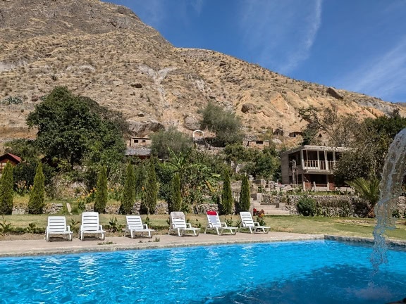 Um pequeno oásis no cânion do Colca com uma piscina com cadeiras brancas para banhos de sol e uma vista panorâmica das montanhas peruanas ao fundo