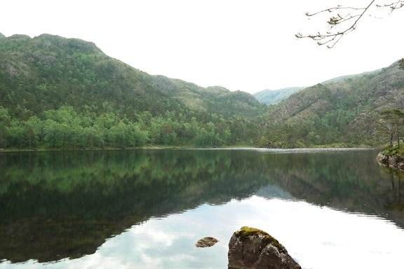 Beira do lago escandinavo com montanhas refletidas na superfície calma do lago