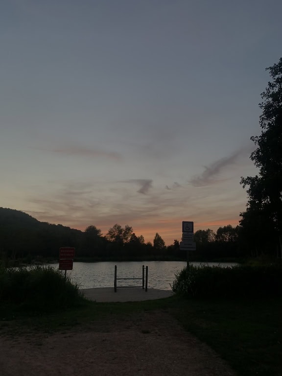 Lake with a small dock and a signs next to it at dusk