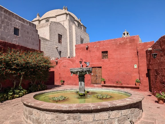 O fântână într-o curte cu biserică cu cupolă în fundal, la mănăstirea Santa Catalina de Siena din Arequipa din Peru