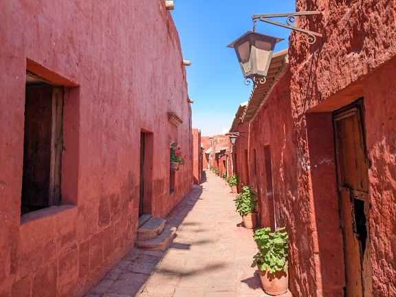 Wąska uliczka z czerwonymi domami i lampą przy drzwiach wejściowych w klasztorze Dominikanów Drugiego Zakonu Santa Catalina de Siena w Arequipie w Peru