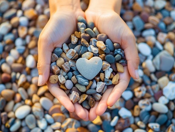 A person holding a heart-shaped stone on top of other pebbles in the palms of their hands, an illustration of finding love