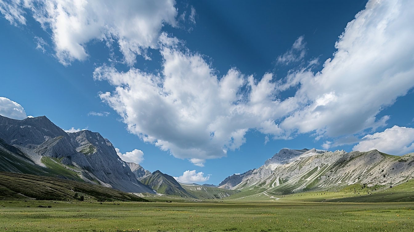 Una valle con campo verde con cielo azzurro con nuvole e montagne sullo sfondo