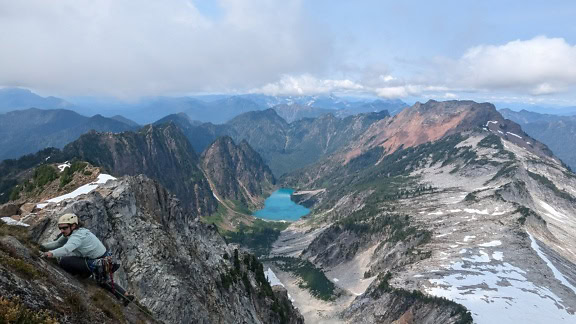 A professional sport mountaineering climber climbs a mountain range with a majestic landscape of lake and mountains in the background