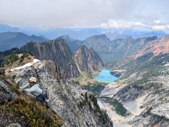 Egy férfi felmászik egy hegyláncra, panorámával a tóra és a hegyekre a Vesper-csúcson, az Észak-Kaszkádok régiójában, Washingtonban