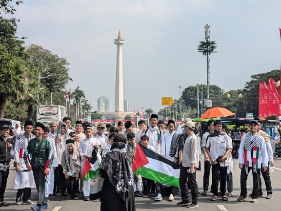 Sekelompok orang berdiri di jalan dengan bendera Indonesia di alun-alun Merdeka, Jakarta, Indonesia