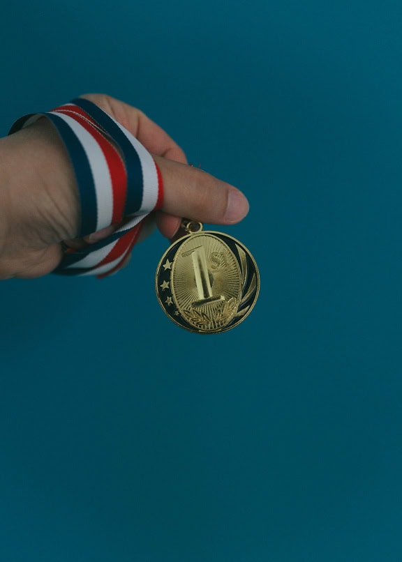 Close-up van de hand van een persoon die een gouden medaille houdt voor het winnen van de 1e plaats in de sportcompetitie