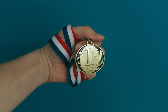 La mano sostiene la medalla de oro por ganar el 1er lugar en la competencia deportiva