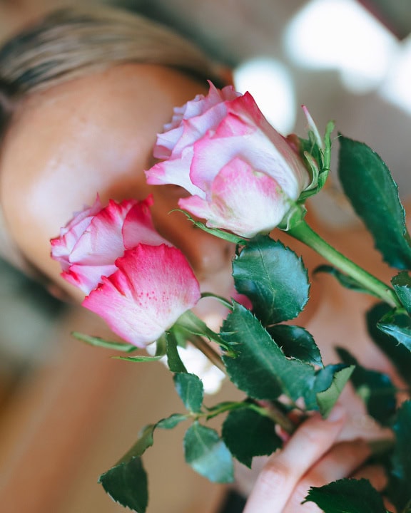 En kvinne som holder rosa roseblomster i ansiktet og dekker øynene