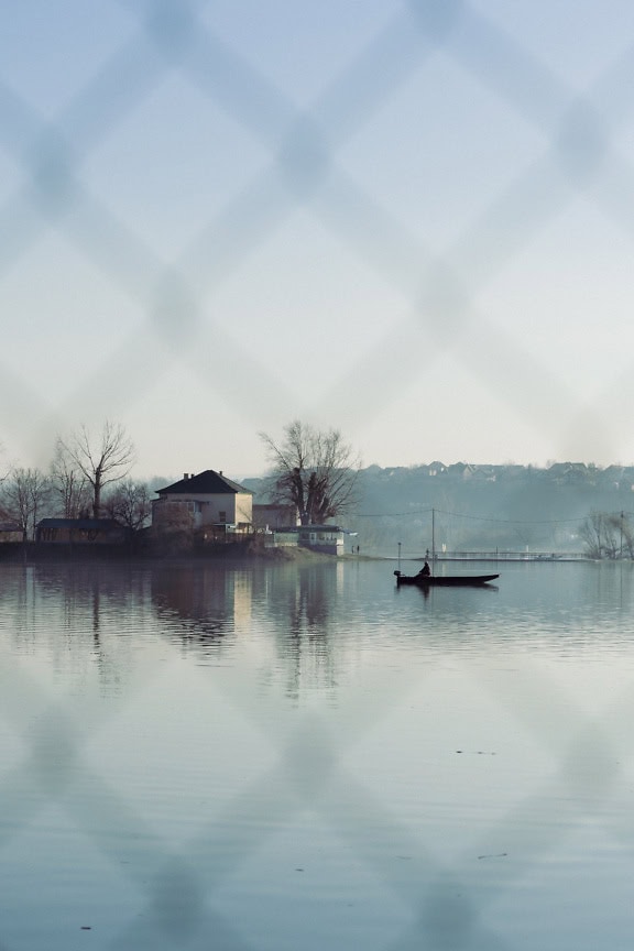 Fotografie a unei bărci mici pe apă fotografiată prin gard de sârmă