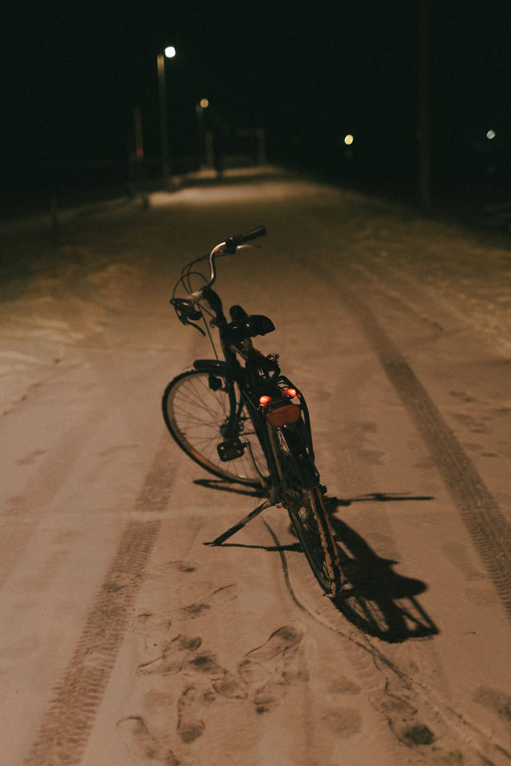 Bicycle parked on a snowy road under street light at night