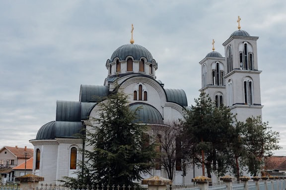 The Orthodox church with two towers of the Holy Apostles Peter and Paul with a fence and trees