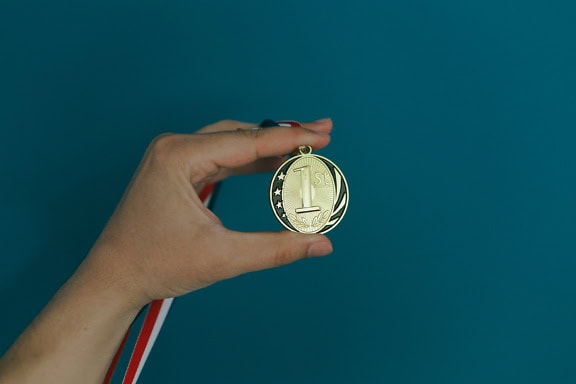 A hand holding a gold medal, a dream of an Olympic games, an illustration of sport champion wining 1st place on a sport tournament or championship