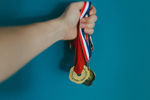 A hand holds gold medals, an illustration of achieving sport successes and wining sport tournaments and championships