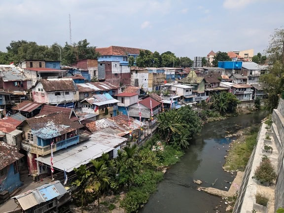 Sungai yang mengalir melalui kota kumuh, pemandangan udara daerah pedesaan yang padat penduduk dengan rumah-rumah miskin di Jawa di Indonesia