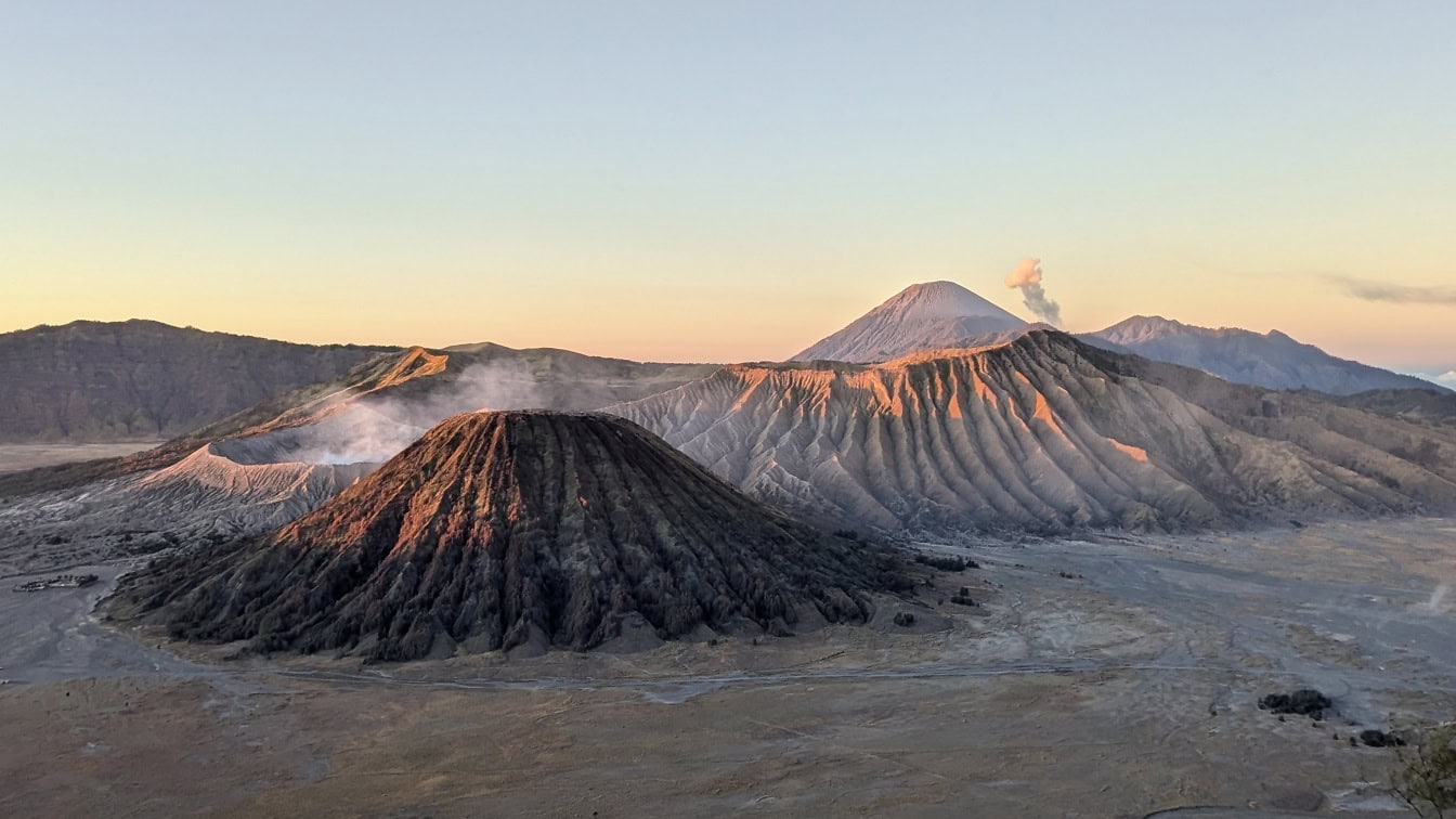 En fjellkjede med en Bromo-vulkan med røyk som kommer ut av vulkankrateret ved solnedgangen