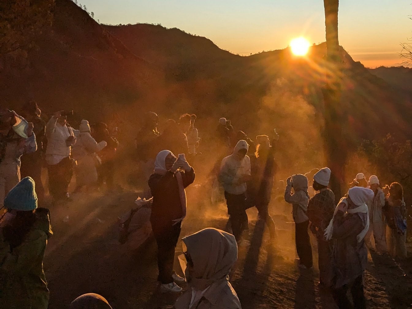 Skupina lidí stojících na zemi v prachu při západu slunce na hoře Bromo, turistické atrakci v Indonésii