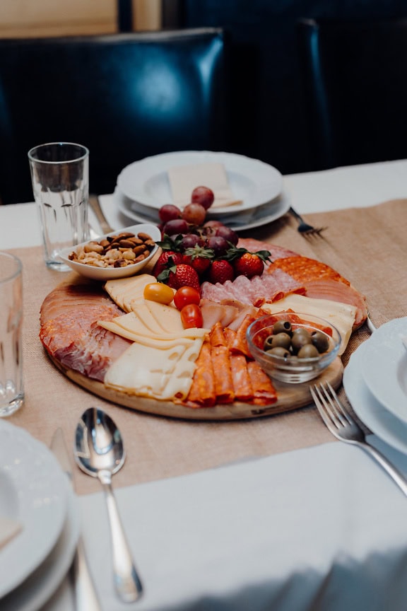 Teller mit Speisen auf einem Tisch mit frischen roten Trauben, Oliven, Käse und Würstchen mit Schweinefleisch