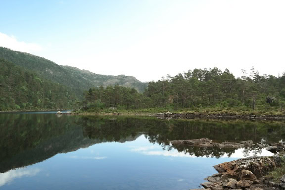 En blåvit himmel över fantastisk sjö i Norge med träd och berg i bakgrunden