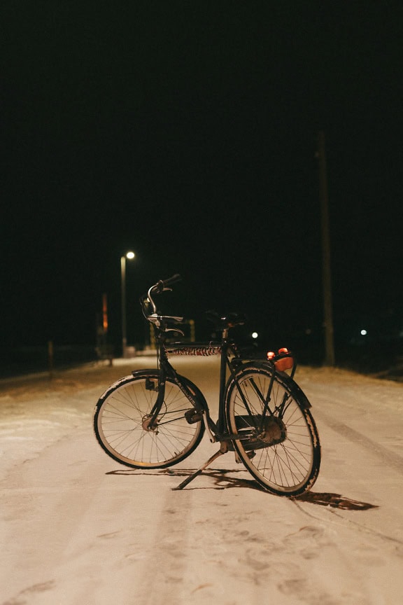 Bicicletta nera parcheggiata su una strada innevata sotto il lampione di notte