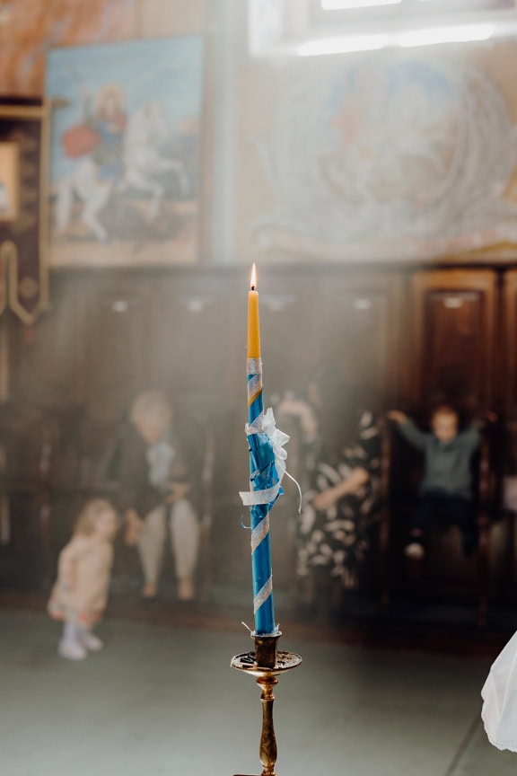 A yellow candle wrapped in a blue ribbon, a church candle used during a religious wedding, baptism, or coronation liturgy in a Christian church