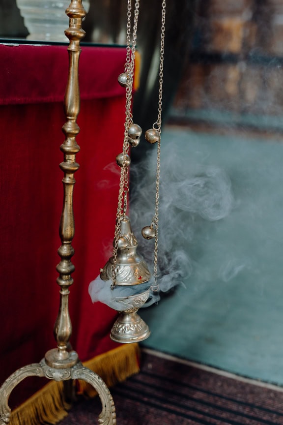 A silver censer with smoke coming out of it, an ecclesiastical object used in the Orthodox or Catholic church during a religious liturgy