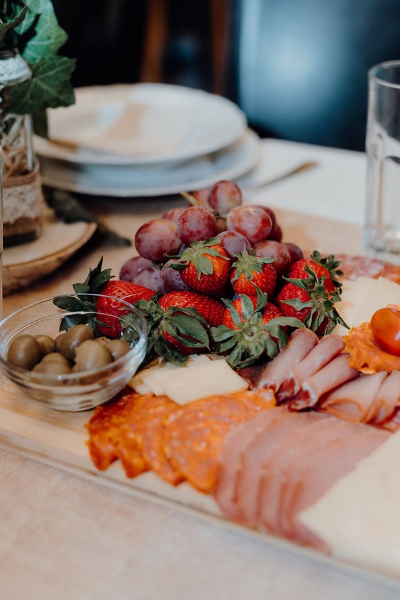 Plate of food on a table with fresh red grapes, strawberries and pork sausage, ham and cheese