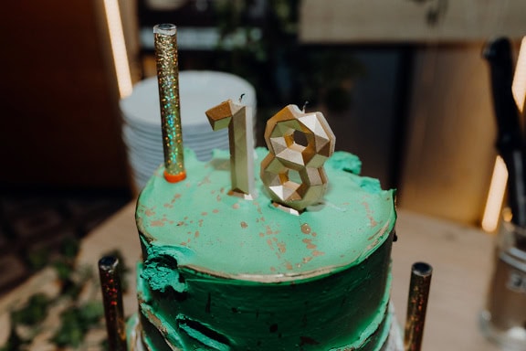 Green birthday cake with a candle in shape of number eighteen (18) on top, a cake to celebrate an adult age