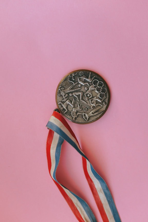 Een bronzen medaille op roze achtergrond met een rood wit en blauw lint, prijs voor het winnen van de 3e plaats in de competitie