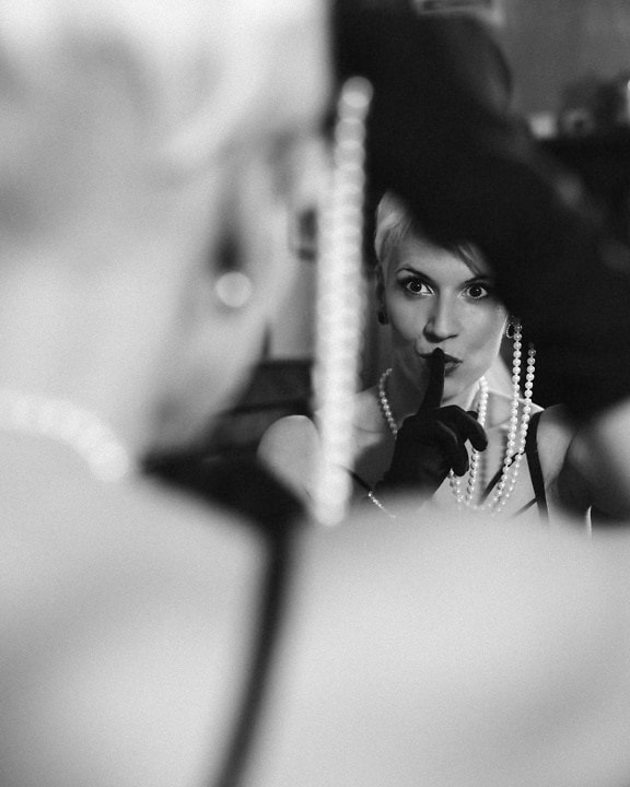 Una mujer con un collar de perlas y guantes negros se mira en el espejo, una hermosa foto de retrato en blanco y negro