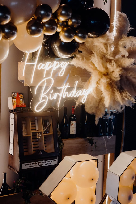 Lit up neon Happy Birthday sign with balloons and a wine bottles at birthday party in a night club