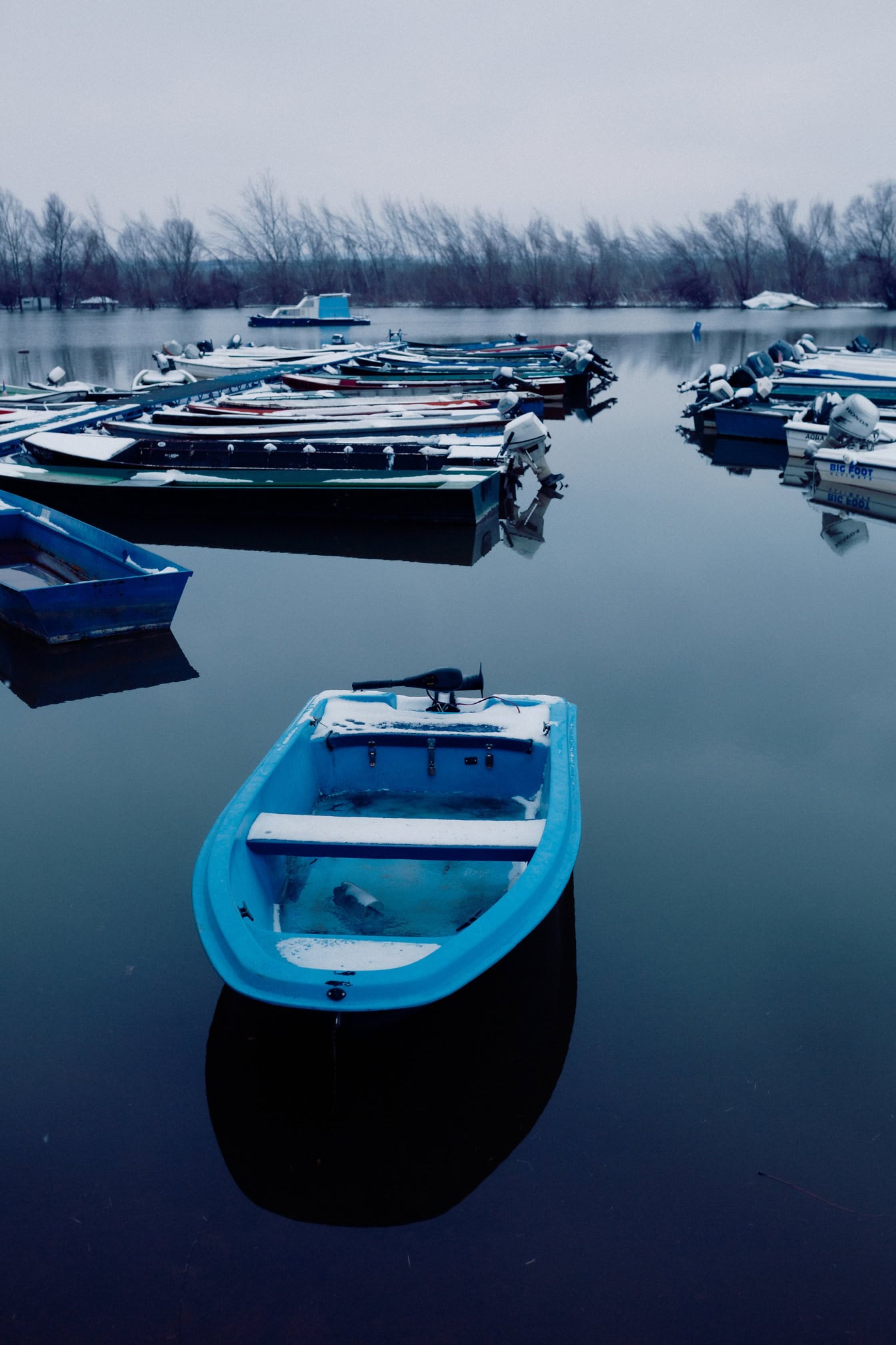 Schneebedeckte Fischerboote im kalten Wasser am kleinen Hafen am See im Winter