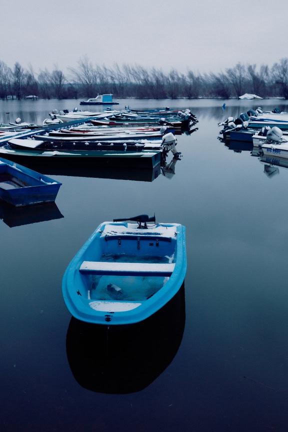 Schneebedeckte Fischerboote im kalten Wasser am kleinen Hafen am See im Winter