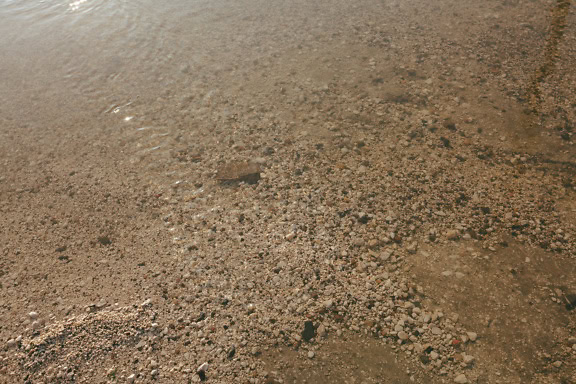 Sandstrand mit kleinen Kieselsteinen im Wasser am Fuße des Flussbettes