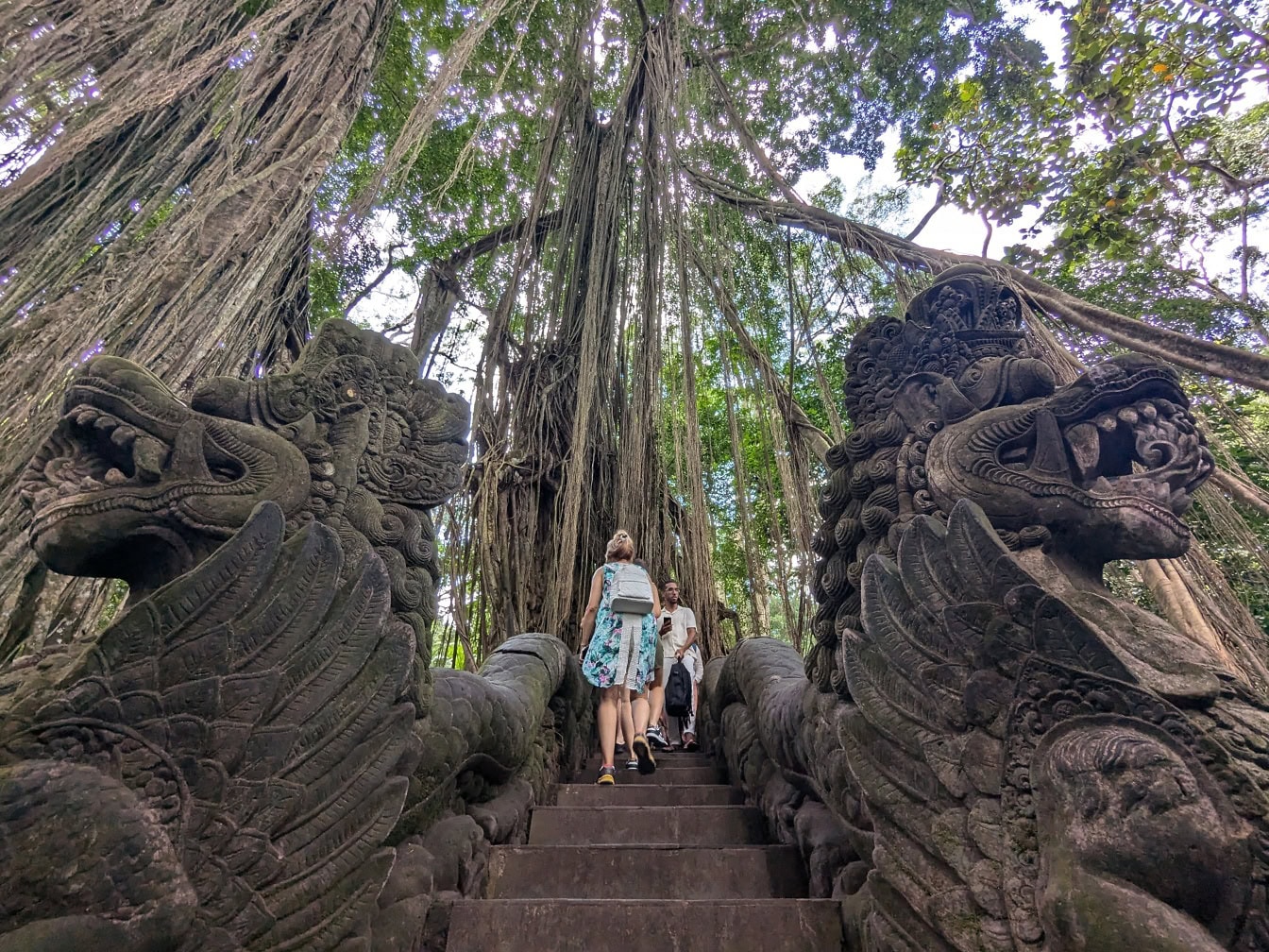 Pessoas subindo uma escada de pedra decorada com esculturas de dragão na Floresta Sagrada dos Macacos de Ubud em Bali, Indonésia