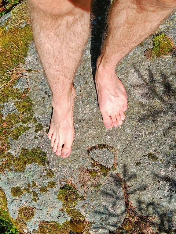 Barfüßige Person, die auf einem moosbewachsenen Felsen steht