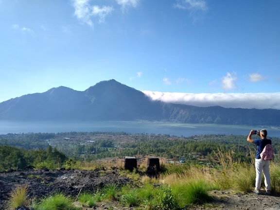 Een toerist op gezichtspunt die een panoramische foto van het landschap met meer en bergketen neemt