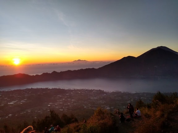 Ľudia sediaci na kopci s výhľadom na západ slnka na hore Batur, aktívnej sopke na Bali v Indonézii