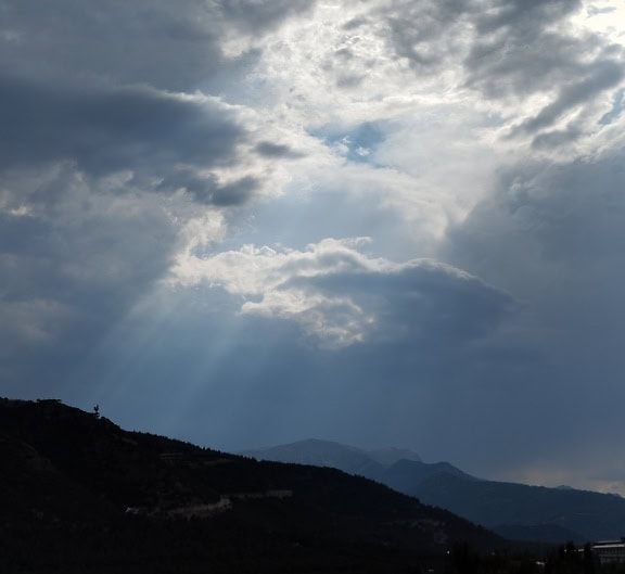 Il sole splende attraverso le nuvole bianche sopra le montagne