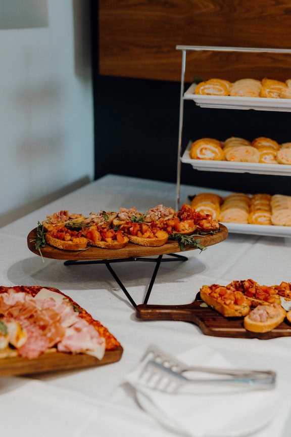 Bandejas de comida de café da manhã na mesa, uma tábua de madeira com deliciosos sanduíches, pãezinhos de queijo e fatias de presunto e salsicha