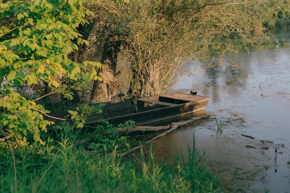 Foto da paisagem de um barco de pesca de madeira velho na água na margem de um lago na mola