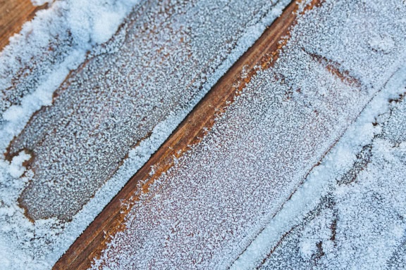 木头表面上冻结的雪的纹理，对角线堆叠的木板覆盖着雪