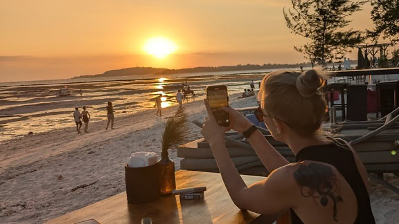 Nainen ottamassa älypuhelimellaan kuvaa rannasta auringonlaskun aikaan