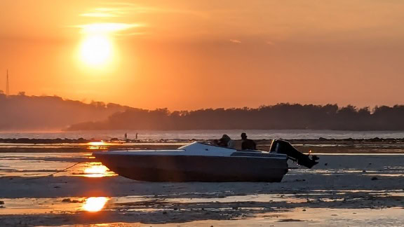 Boot bei Ebbe bei Sonnenuntergang an einem Sandstrand gestrandet