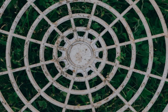 Texture of a white circular plastic grid made out of a high-strength thermoplastic, a polyvinyl chloride layed down on green plants